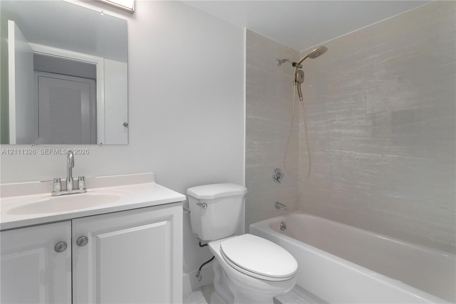 Guest bathroom featuring a vanity with an integrated sink, polished chrome faucet, flat-panel cabinetry, a rectangular wall-mounted mirror, and a bathtub with a tiled surround.