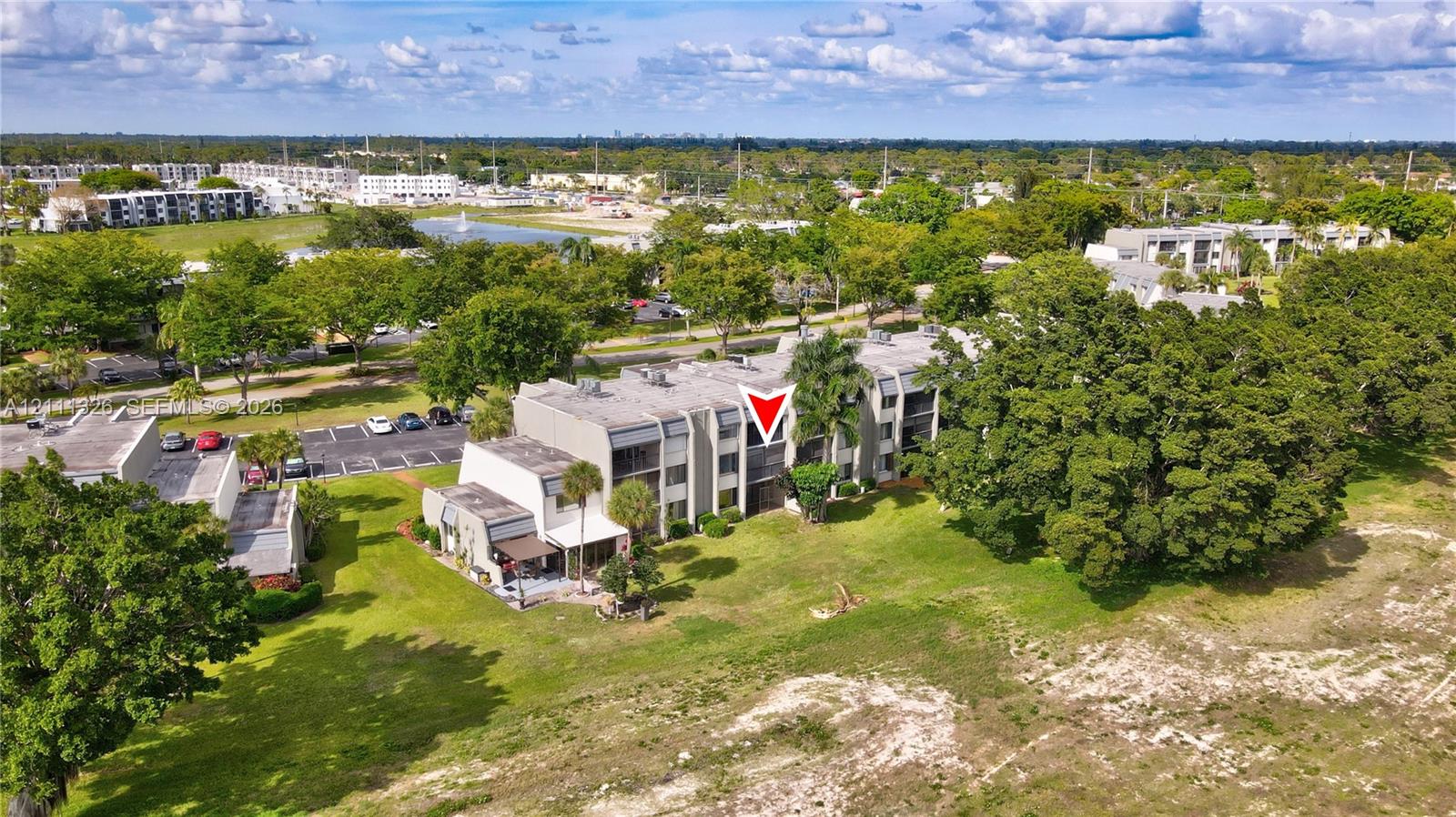 Multi-story residential building featuring concrete construction, flat roofline, private balconies, and surrounding green space with mature trees