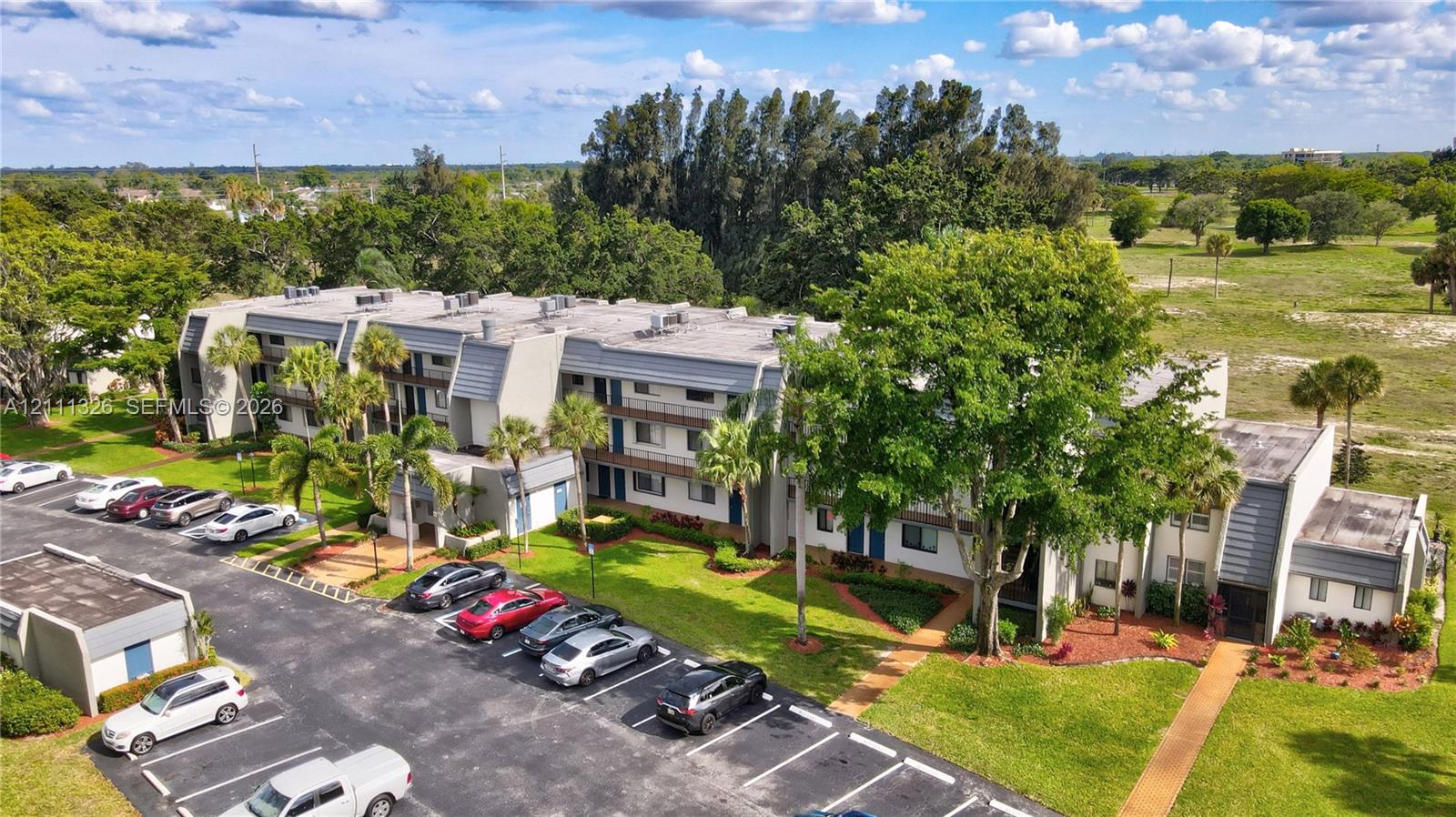 Multi-story exterior featuring paved surface parking and manicured landscaping with mature trees.