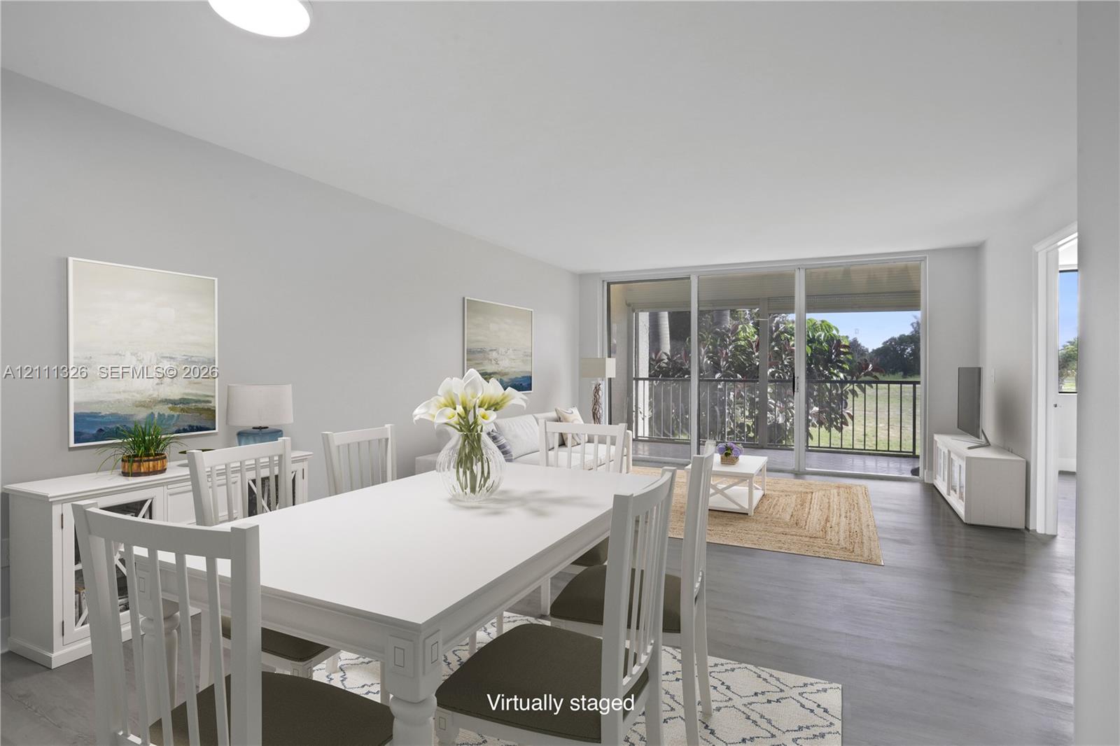 Open-concept interior featuring neutral walls, wood-finish flooring, and sliding glass doors leading to a covered screened-in balcony. This photo has been virtually staged.