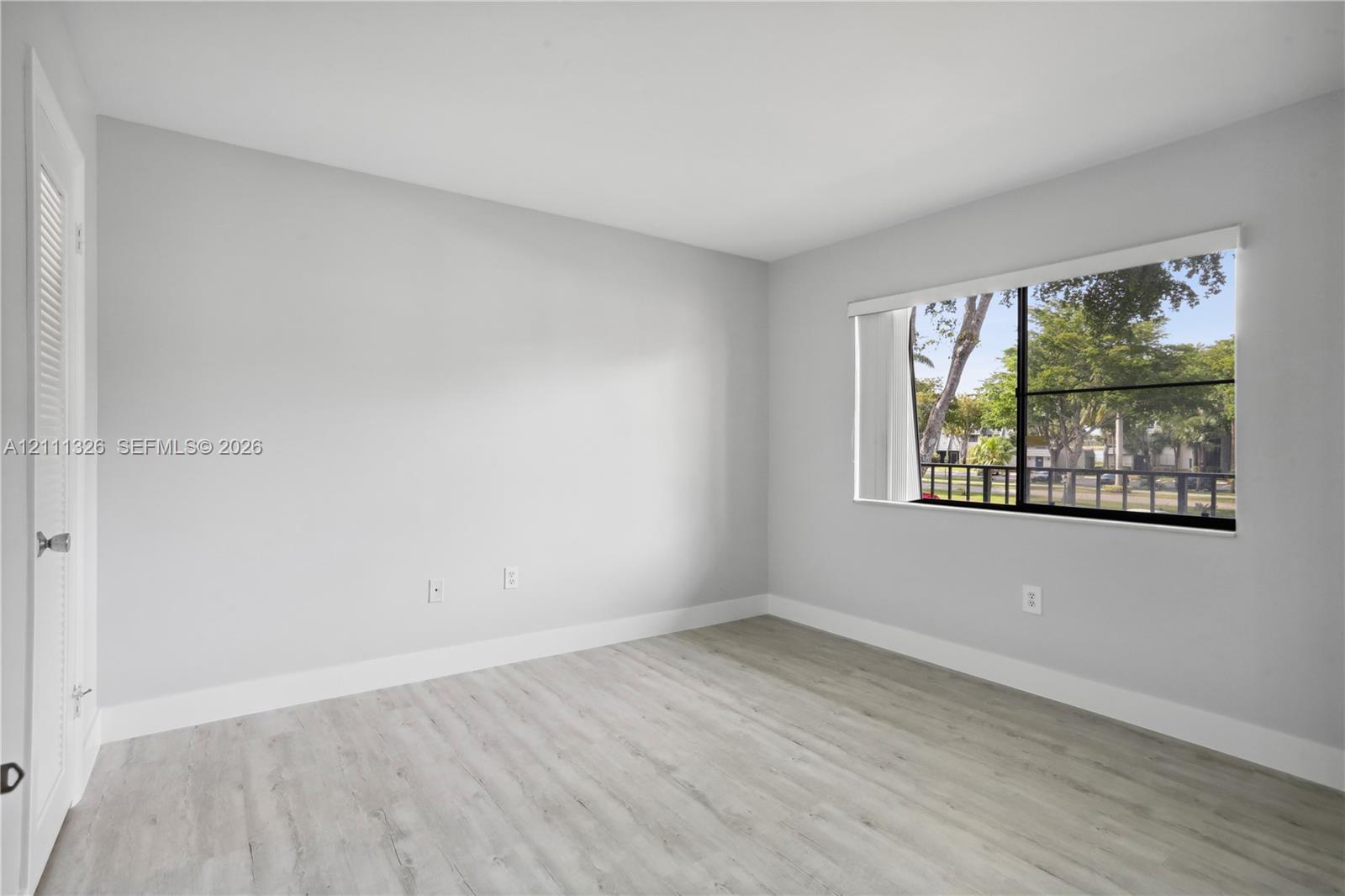 Second bedroom with neutral-toned interior featuring wood-look laminate flooring, a large window with black frames, and a walk-in closet.