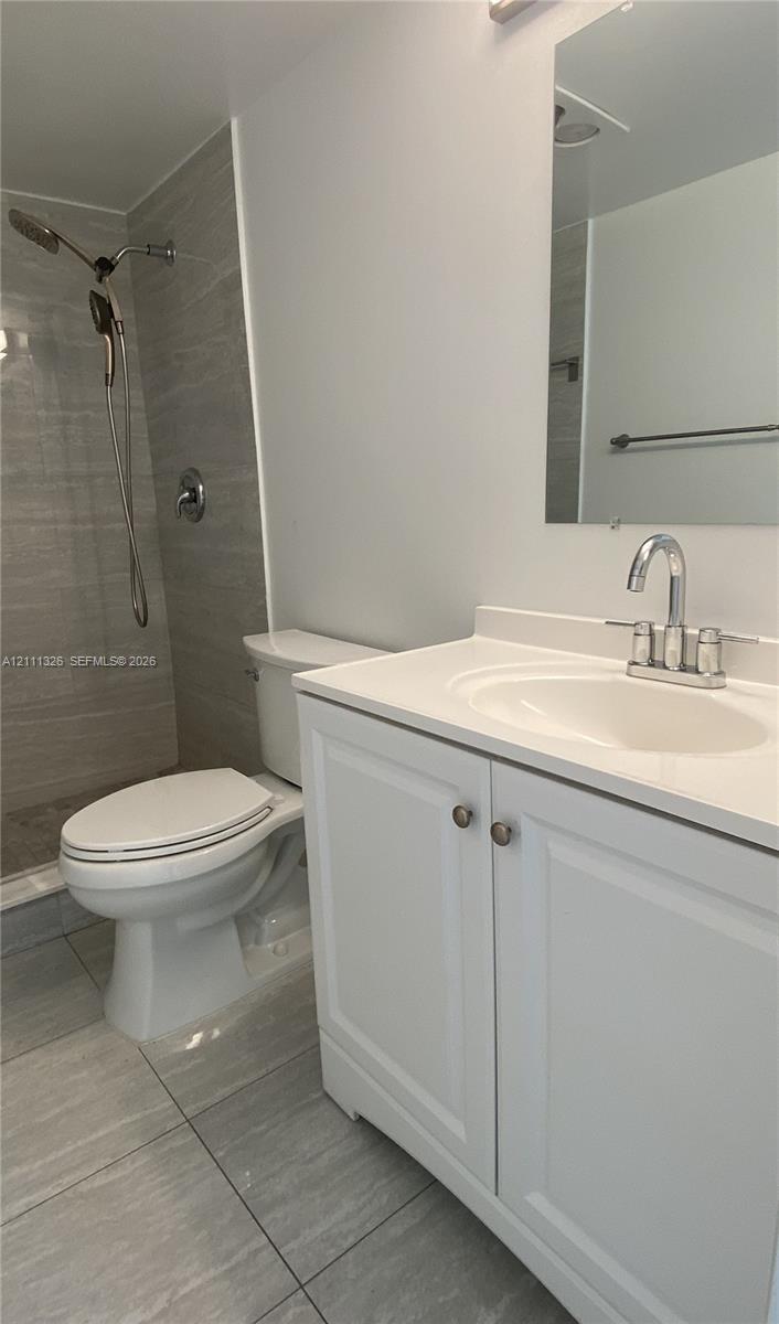 Bathroom featuring a white vanity cabinet with a solid surface countertop, an integrated sink basin, a walk-in shower with horizontal-patterned wall tile, and large-format floor tile