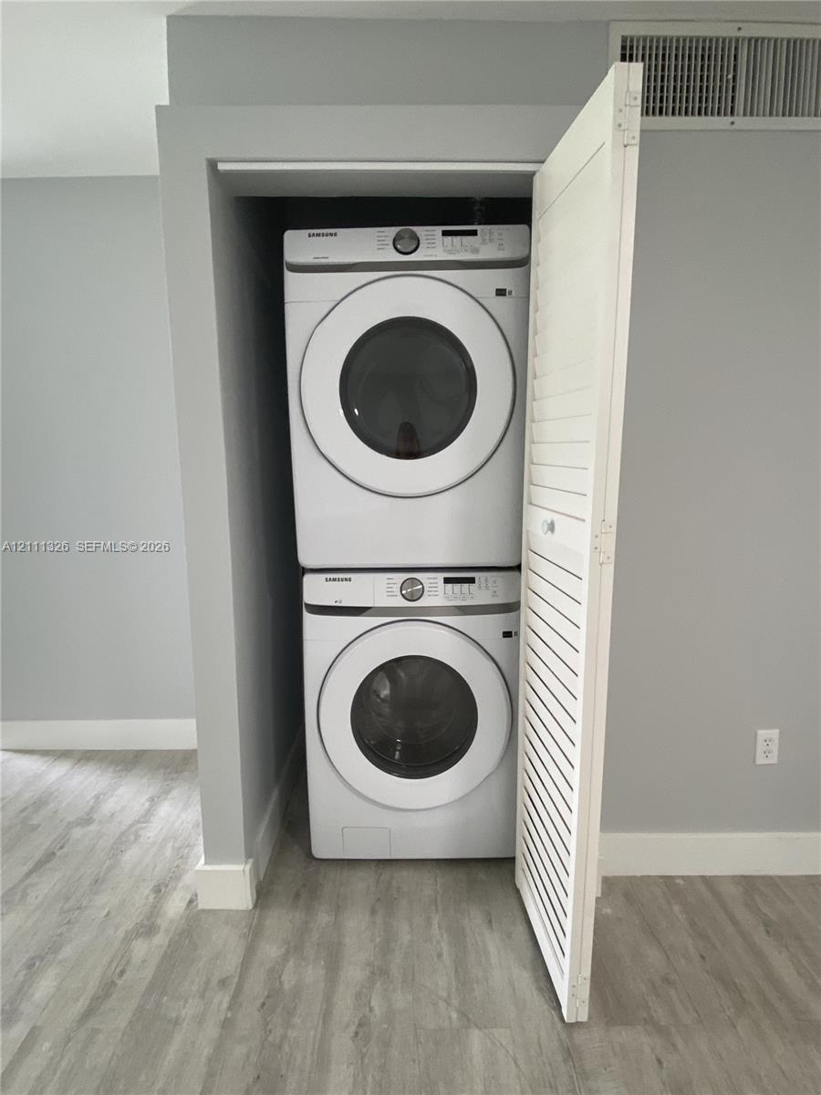 Dedicated laundry alcove featuring stacked, full sized high-capacity front-load washer and dryer units enclosed by a white louvered door