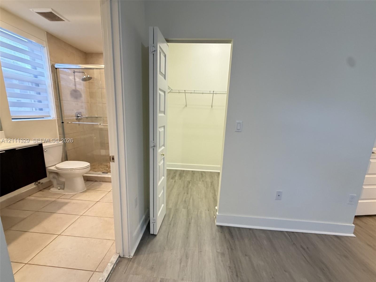 Bathroom featuring a shower with a glass enclosure, wood-finish cabinetry, and tiled flooring, accompanied by a walk-in closet with built-in wire shelving