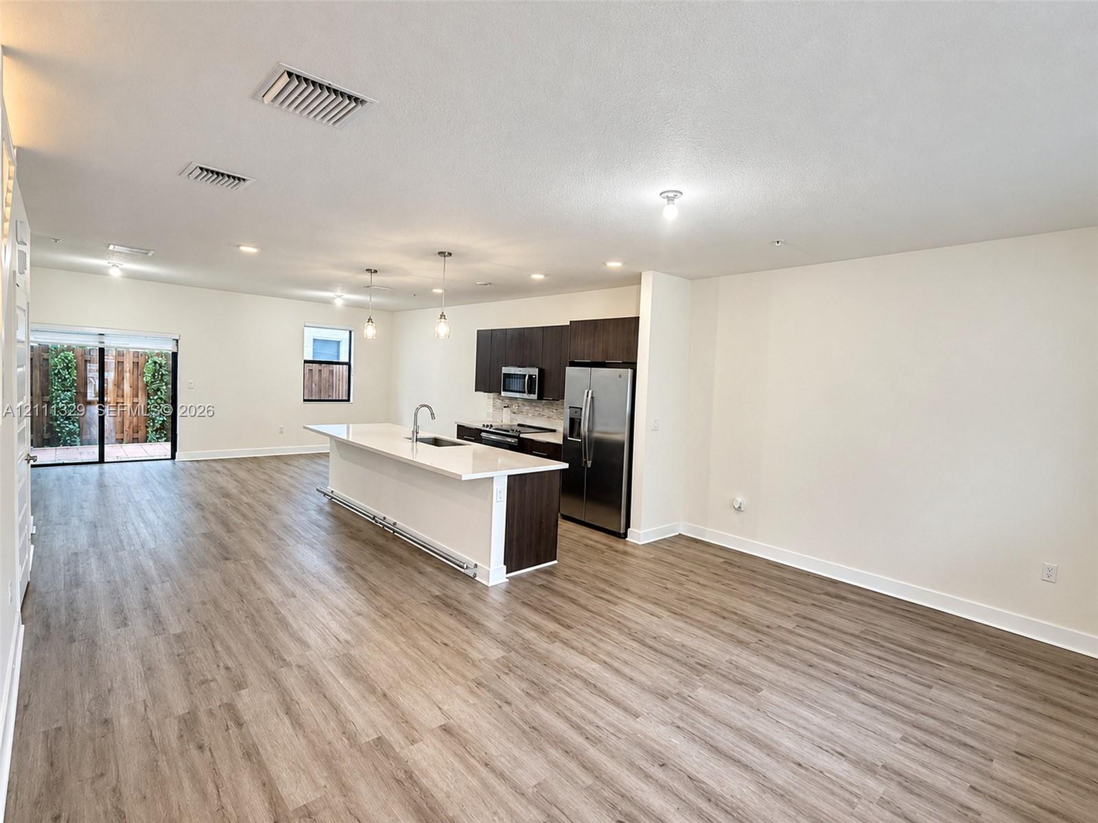 Open-concept kitchen featuring dark wood-finish cabinetry, white stone countertops, an oversized center island, stainless steel appliances, and wood-finish flooring