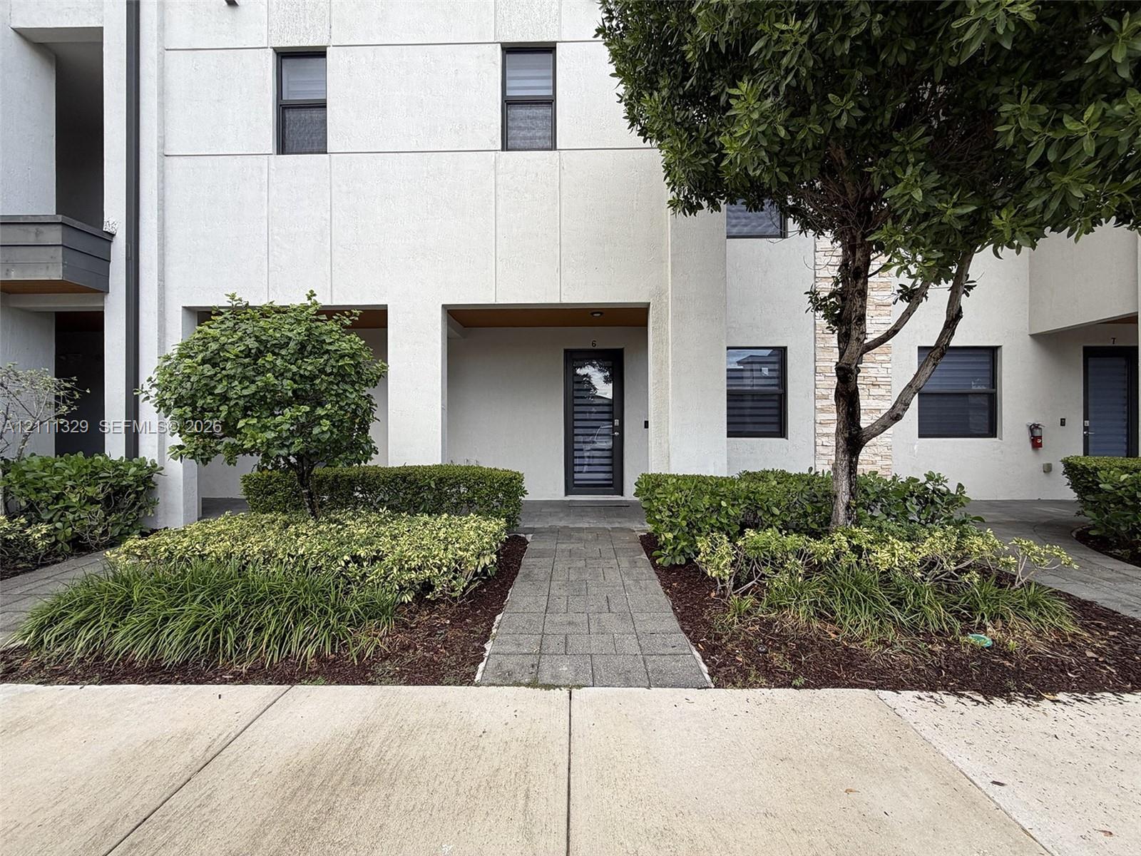 Modern facade with panelized exterior, multi-pane entry door, stone-clad accent wall, stone paver walkway, and manicured shrubbery