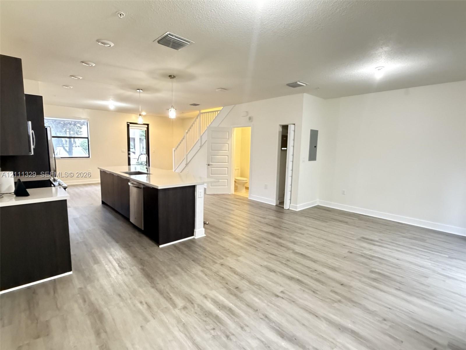 Open-concept floor plan featuring wood-finish flooring, a kitchen island with stone-surface countertops, dark-tone cabinetry, and recessed lighting