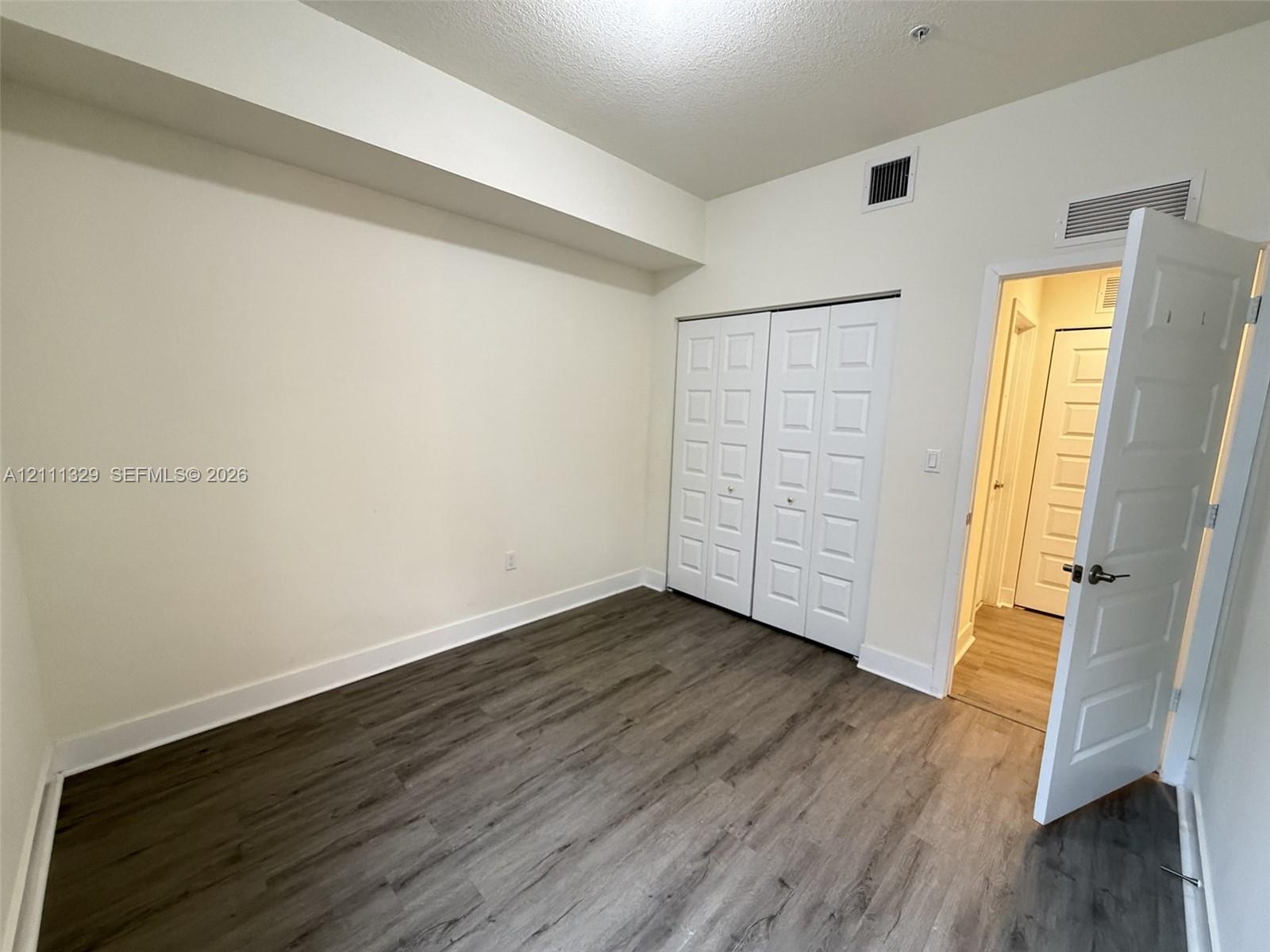 Room featuring wood-finish flooring, recessed ceiling design, and dual-panel closet doors