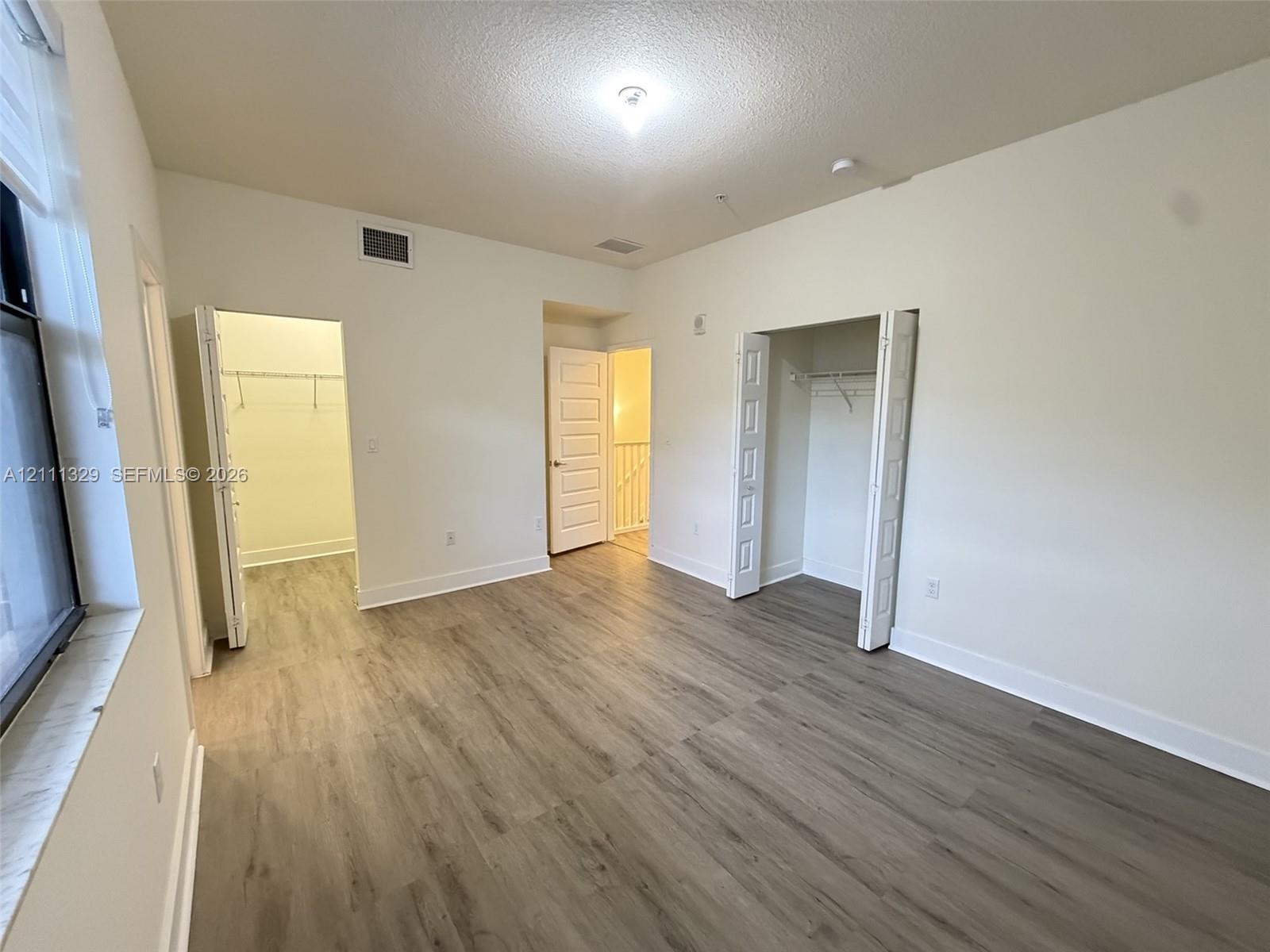 Room with neutral wall finish, wood-finish flooring, two bi-fold door closets, and a multi-panel interior door