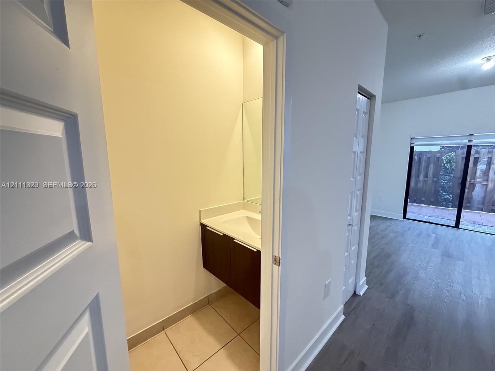 Modern floating vanity with a rectangular sink, white countertop, and dark-finish cabinetry, complemented by tile flooring and a wall-mounted mirror