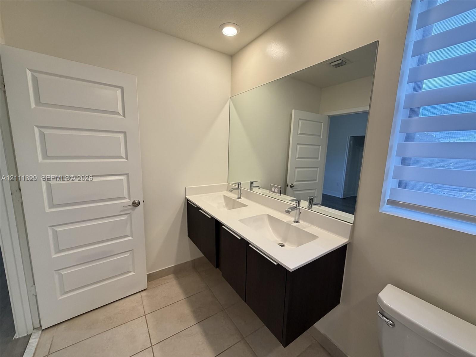 Floating dual-sink vanity with dark cabinetry, white solid-surface countertop, chrome fixtures, and a wall-to-wall mirror