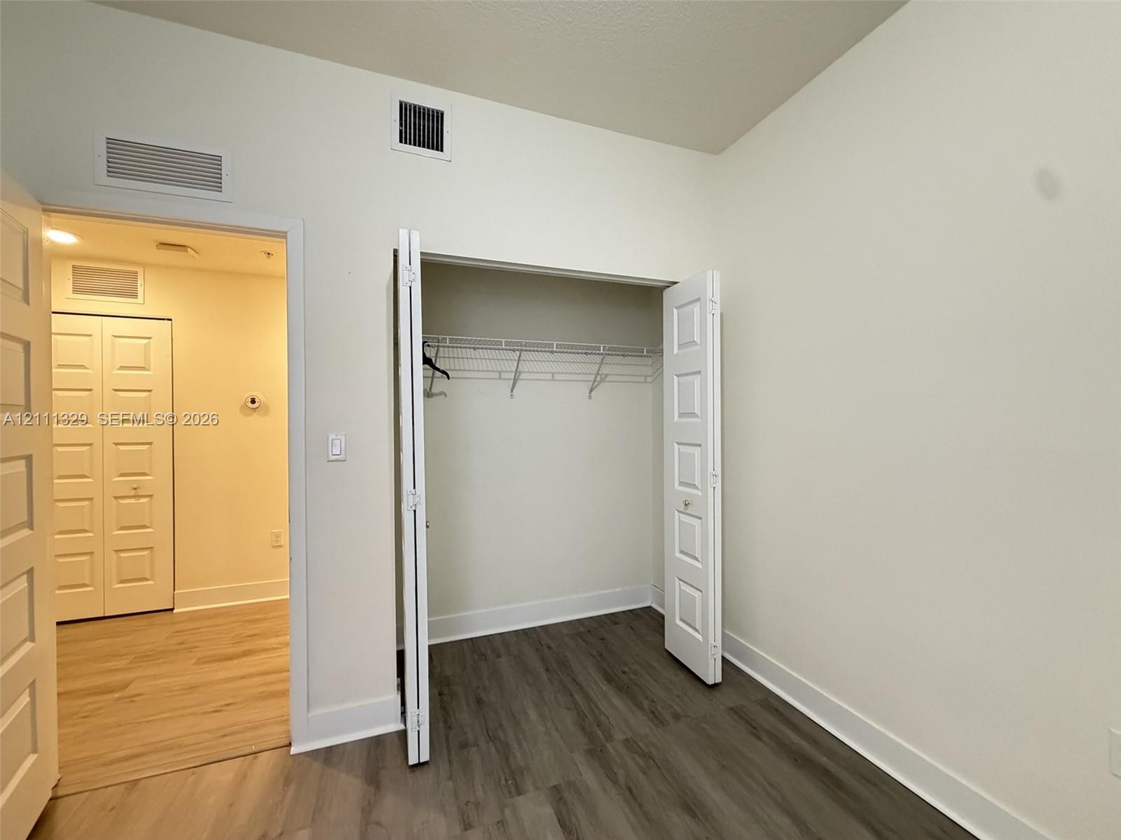 Interior space featuring wood-finish flooring, white five-panel interior doors, and a reach-in closet with integrated wire shelving
