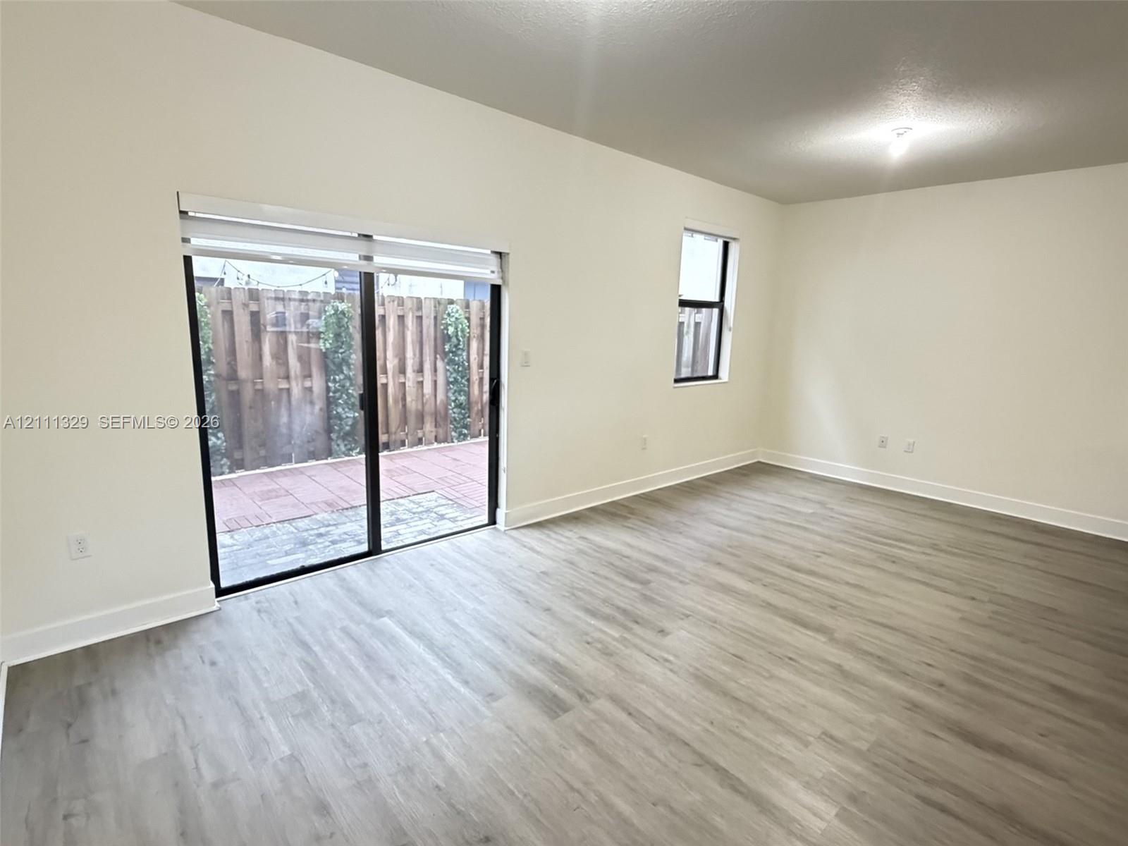 Interior space featuring light-toned wood-finish flooring, sliding glass patio doors, neutral wall palette, and a rectangular window