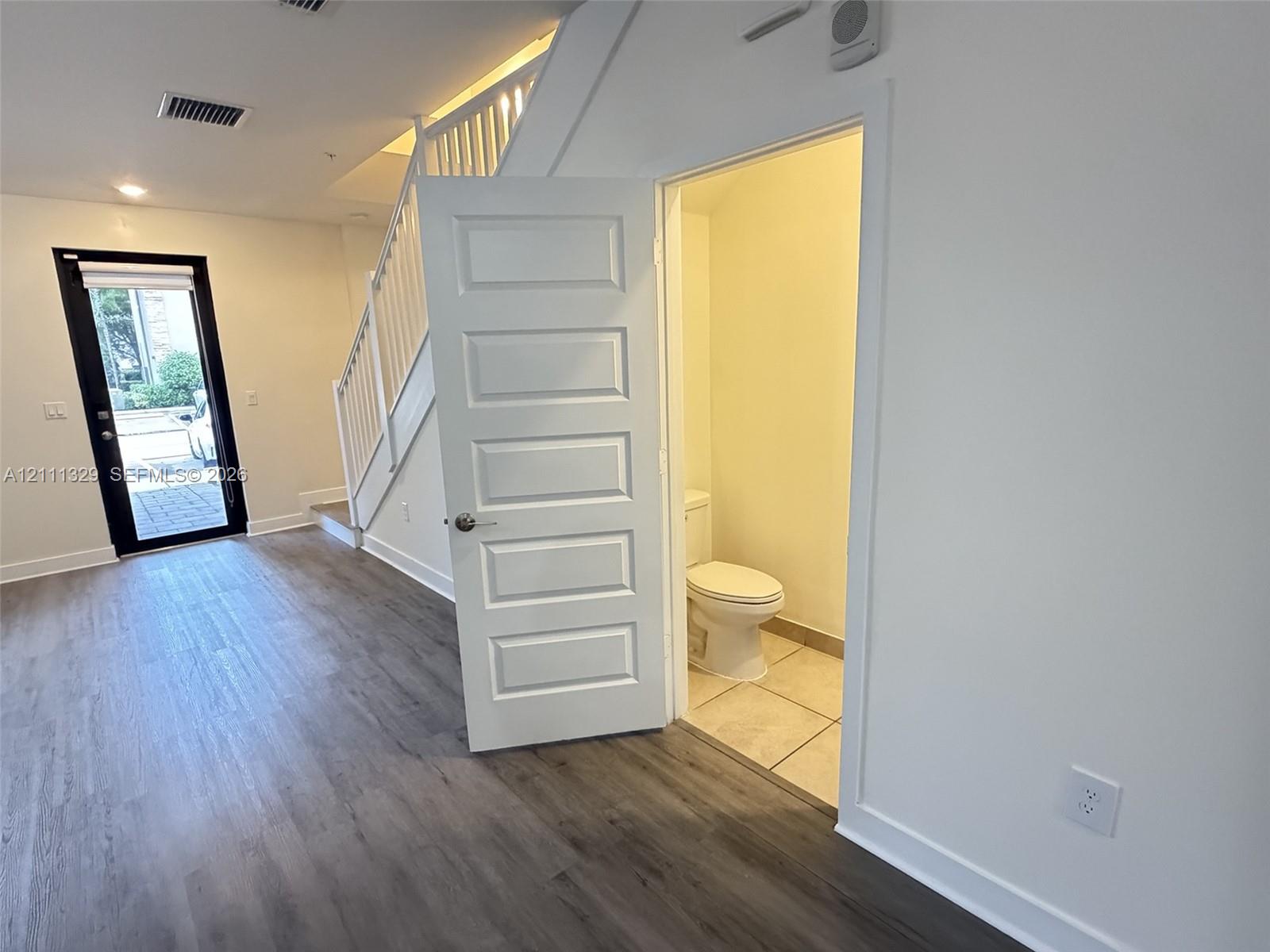 Wood-finish flooring, white staircase railing, paneled interior door, and tile flooring