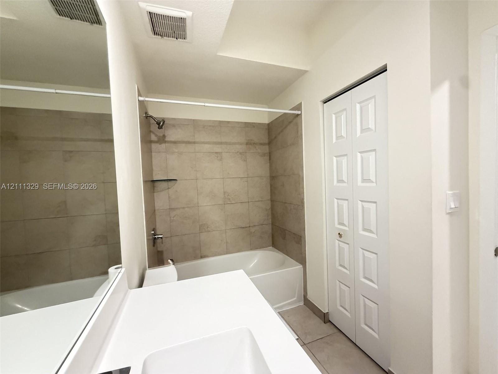 Full-width vanity with a rectangular basin, expansive wall-mounted mirror, white six-panel bifold closet door, and bathtub featuring neutral-toned wall tile