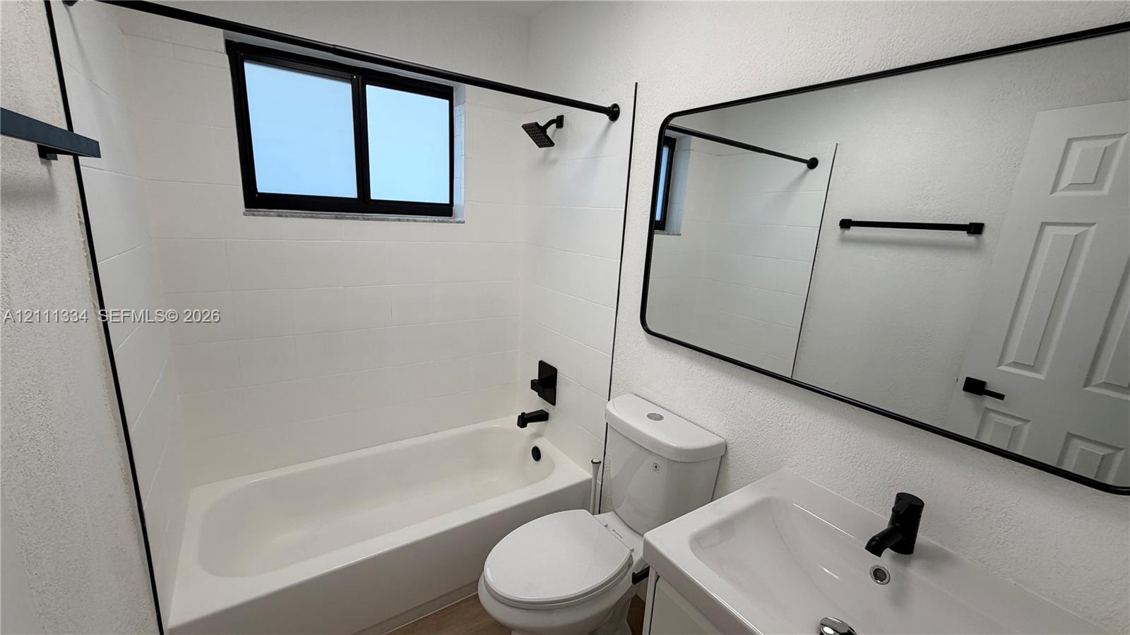 Bathroom featuring a white tub-shower combination, modern matte black fixtures, a wall-mounted mirror with a black frame, and a white vanity