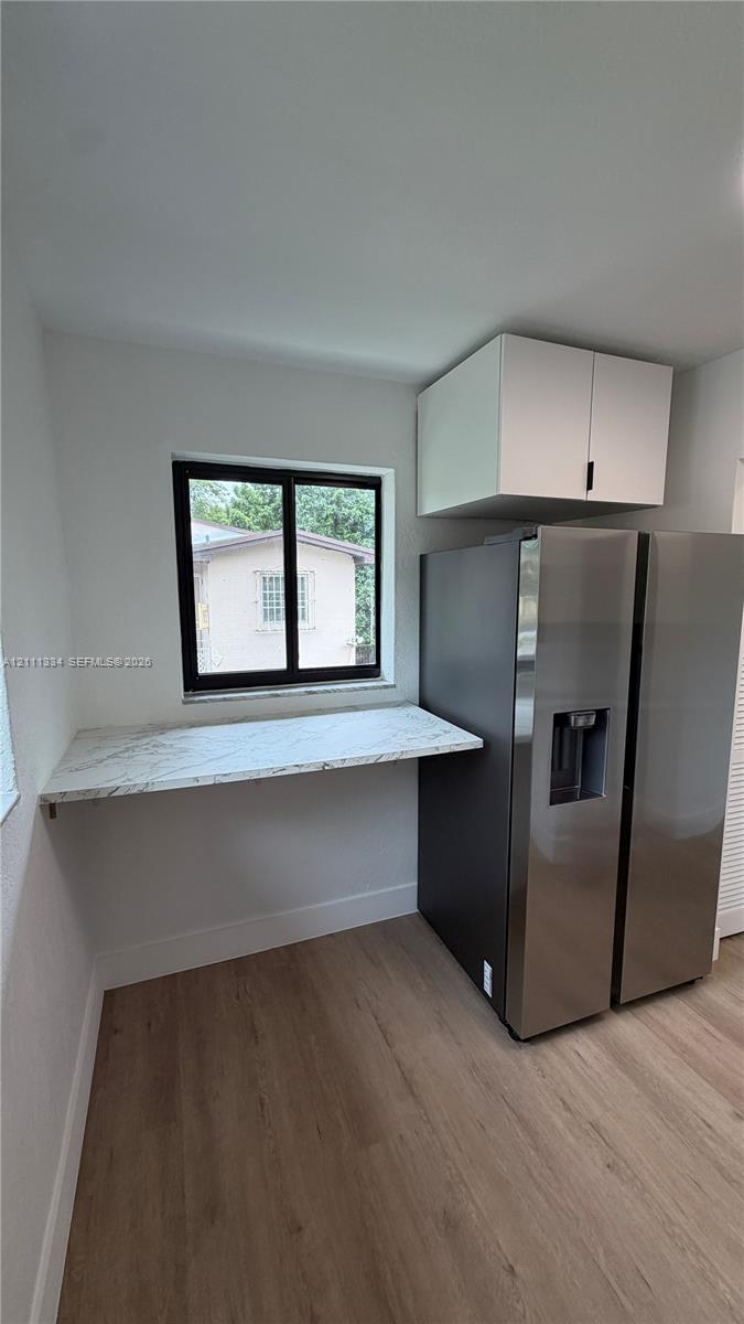 Kitchen nook featuring wood-finish flooring, stone-surfaced counter, stainless steel refrigerator, and overhead cabinetry