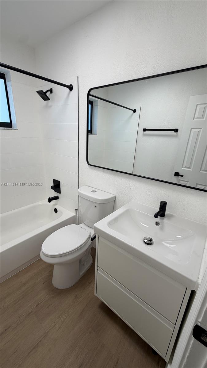 Bathroom featuring a vanity with integrated sink, black matte hardware, framed mirror, and wood-finish flooring