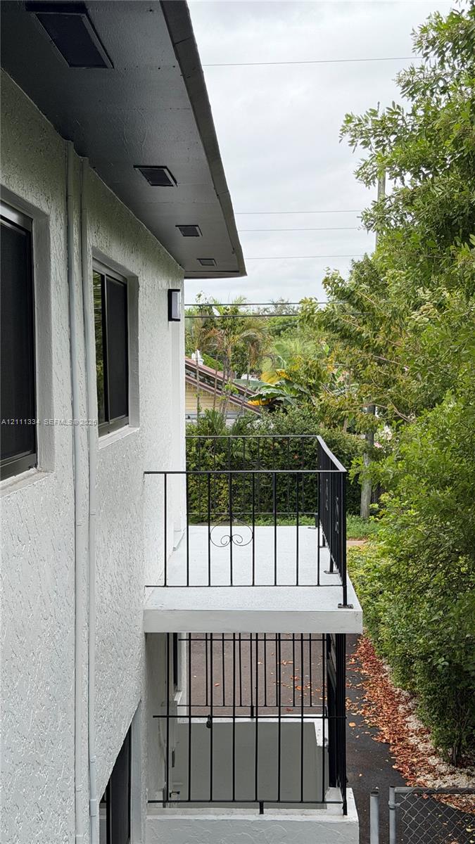 Stucco exterior featuring dual-level outdoor balconies with black metal railings, recessed soffit lighting, and window screens