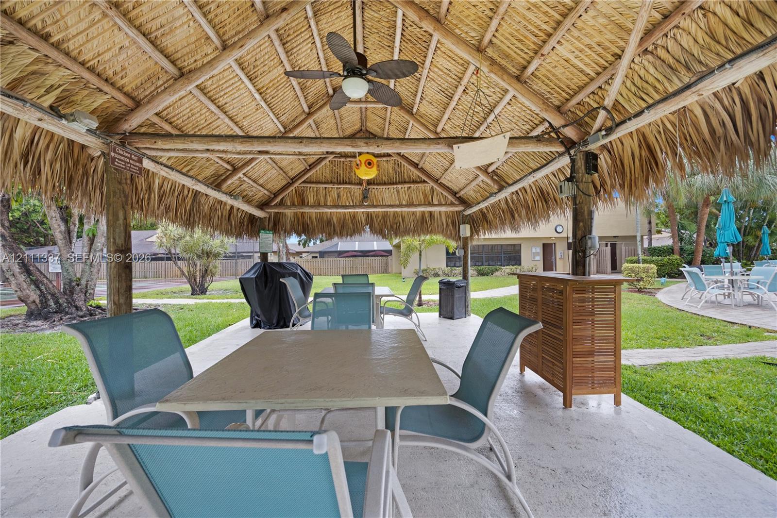 Open-air thatched-roof pavilion featuring a concrete patio, wood support posts, and a ceiling-mounted fan