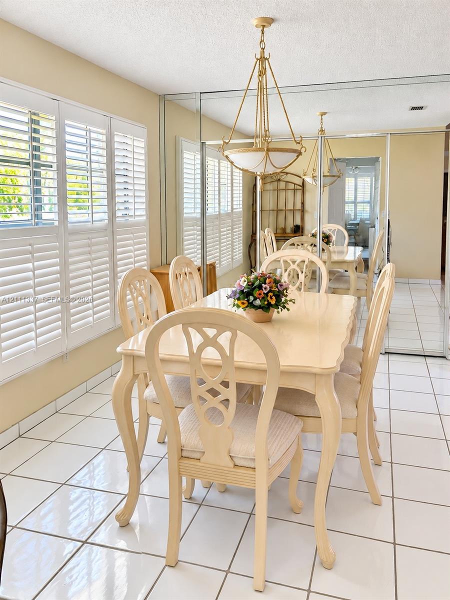 Dining space featuring white ceramic tile flooring, full-wall mirrored panels, plantation shutters, and a multi-arm metal chandelier Dining space featuring white ceramic tile flooring, full-wall mirrored panels, plantation shutters, and a multi-arm metal chandelier
