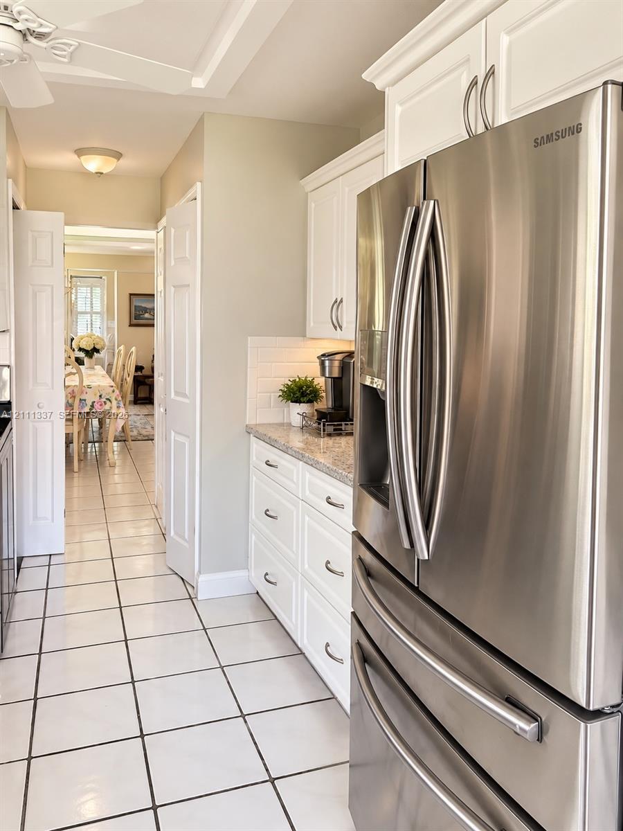 Kitchen featuring white shaker-style cabinetry, stone-finish countertops, subway tile backsplash, stainless steel refrigerator, and tiled flooring Kitchen featuring white shaker-style cabinetry, stone-finish countertops, subway tile backsplash, stainless steel refrigerator, and tiled flooring