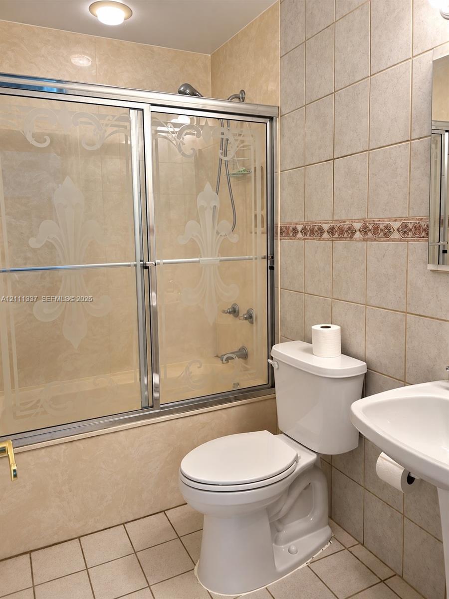 Shower enclosure with decorative etched glass doors, ceramic wall tiling featuring a detailed border accent, and a pedestal sink