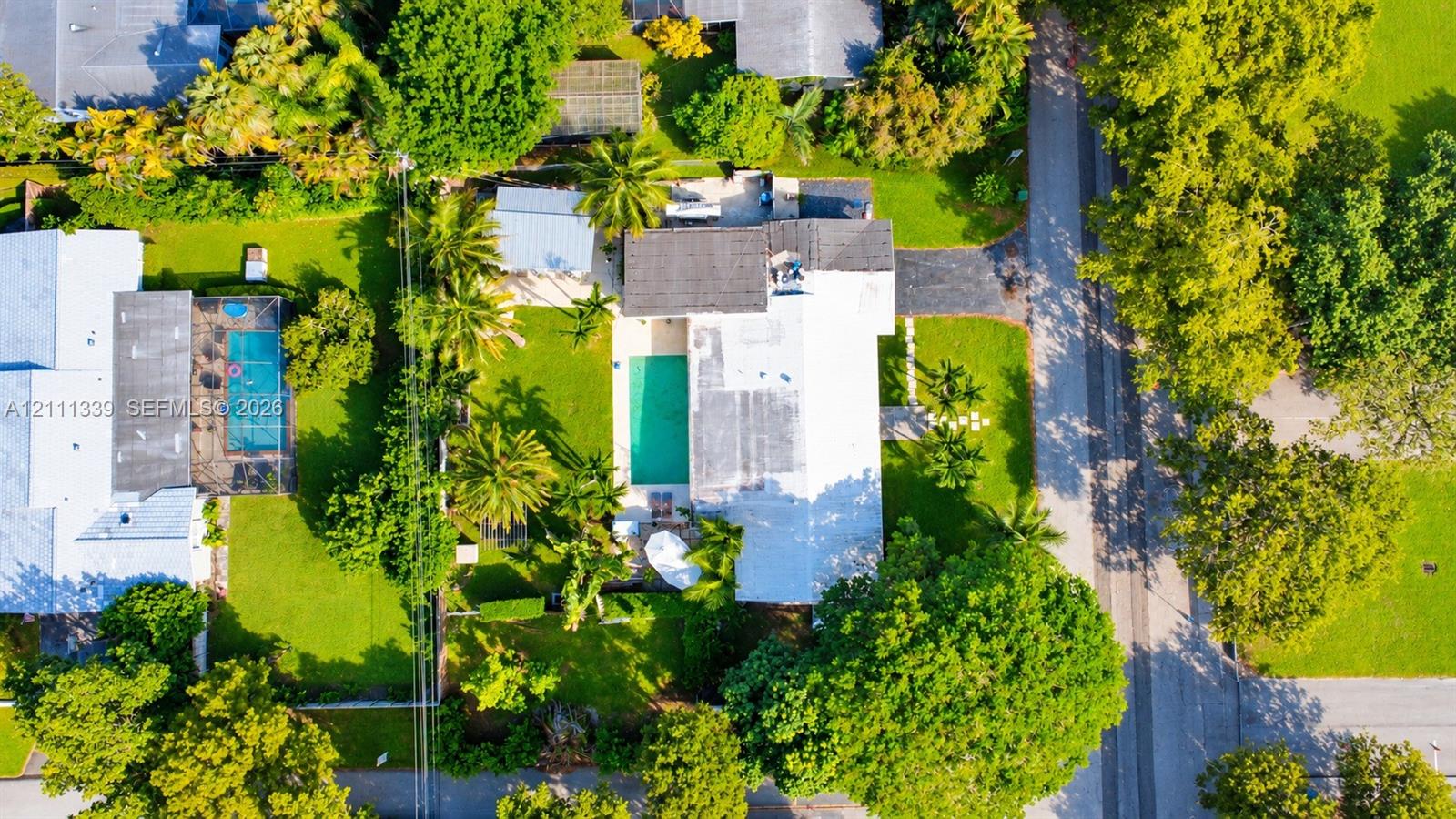 Aerial perspective featuring an inground swimming pool, expansive lawn areas, mature perimeter landscaping, and an asphalt driveway