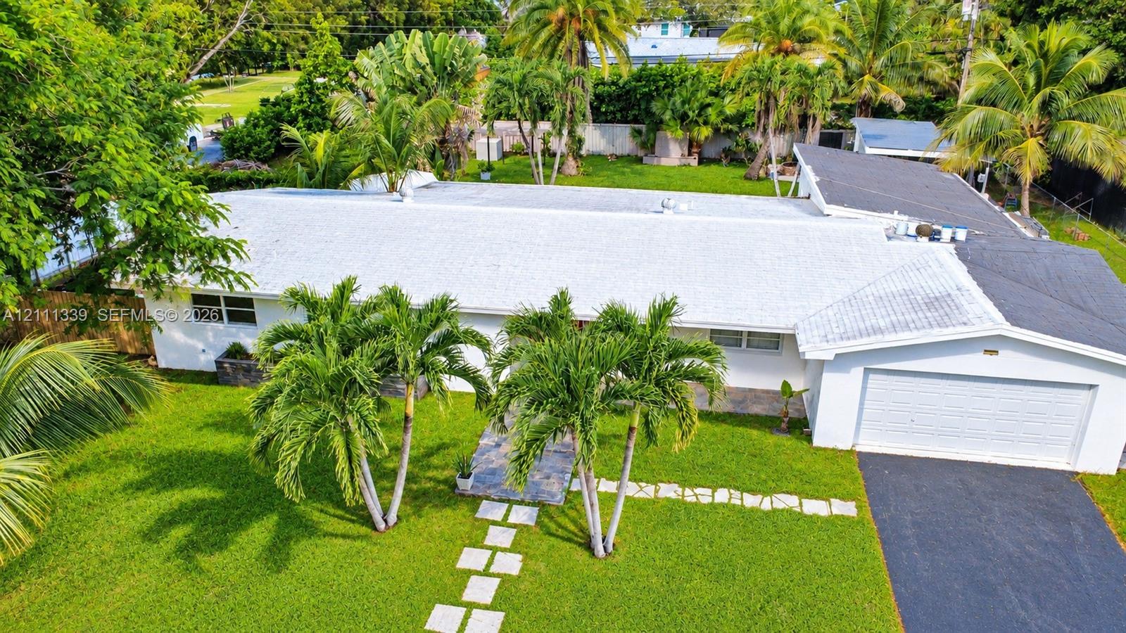 Single-story residence featuring a multi-pitched roof, attached two-car garage, asphalt driveway, stone paver walkway, and mature landscaping