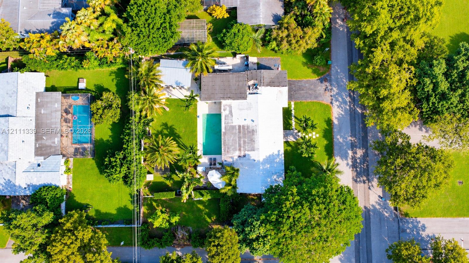 Aerial perspective of property featuring an in-ground swimming pool, expansive green space, mature landscaping, and a paved driveway