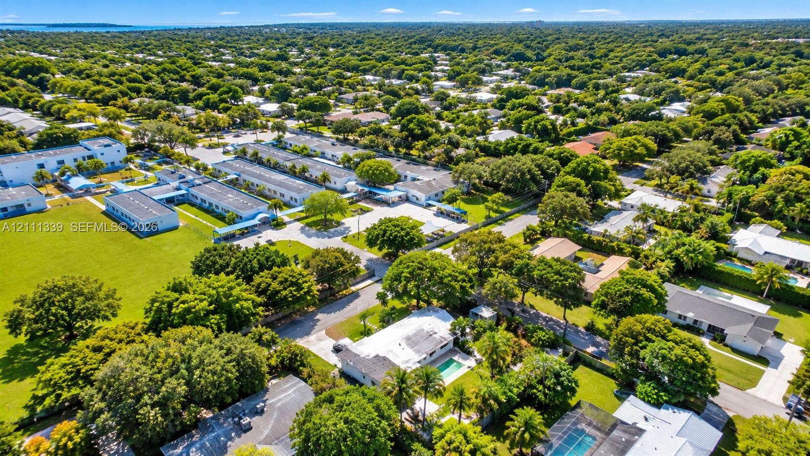 Aerial perspective featuring established residential landscaping, mature tree canopy, and proximity to coastal water