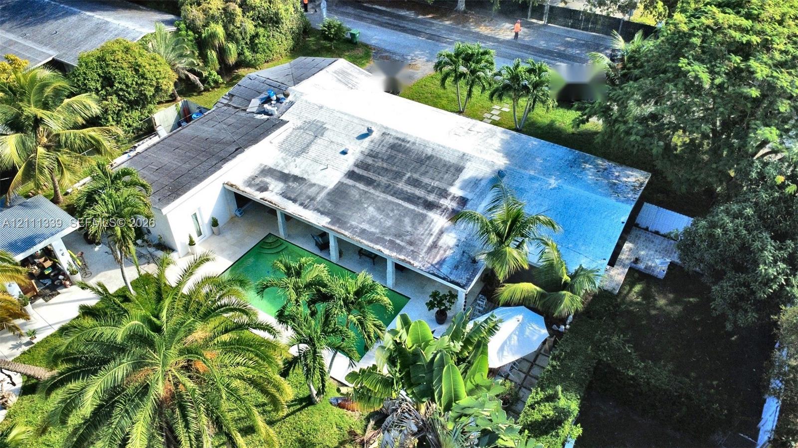 Single-story residence featuring a private swimming pool, covered patio, stone-surfaced hardscaping, and mature palm trees