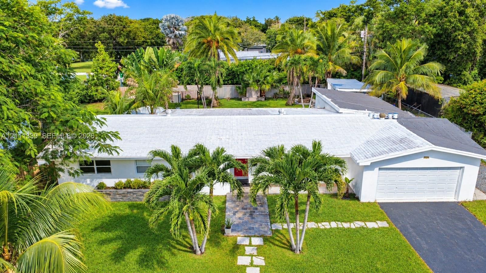 Single-story residence featuring a white exterior, attached two-car garage, asphalt driveway, stone-paver walkway, and mature landscaping
