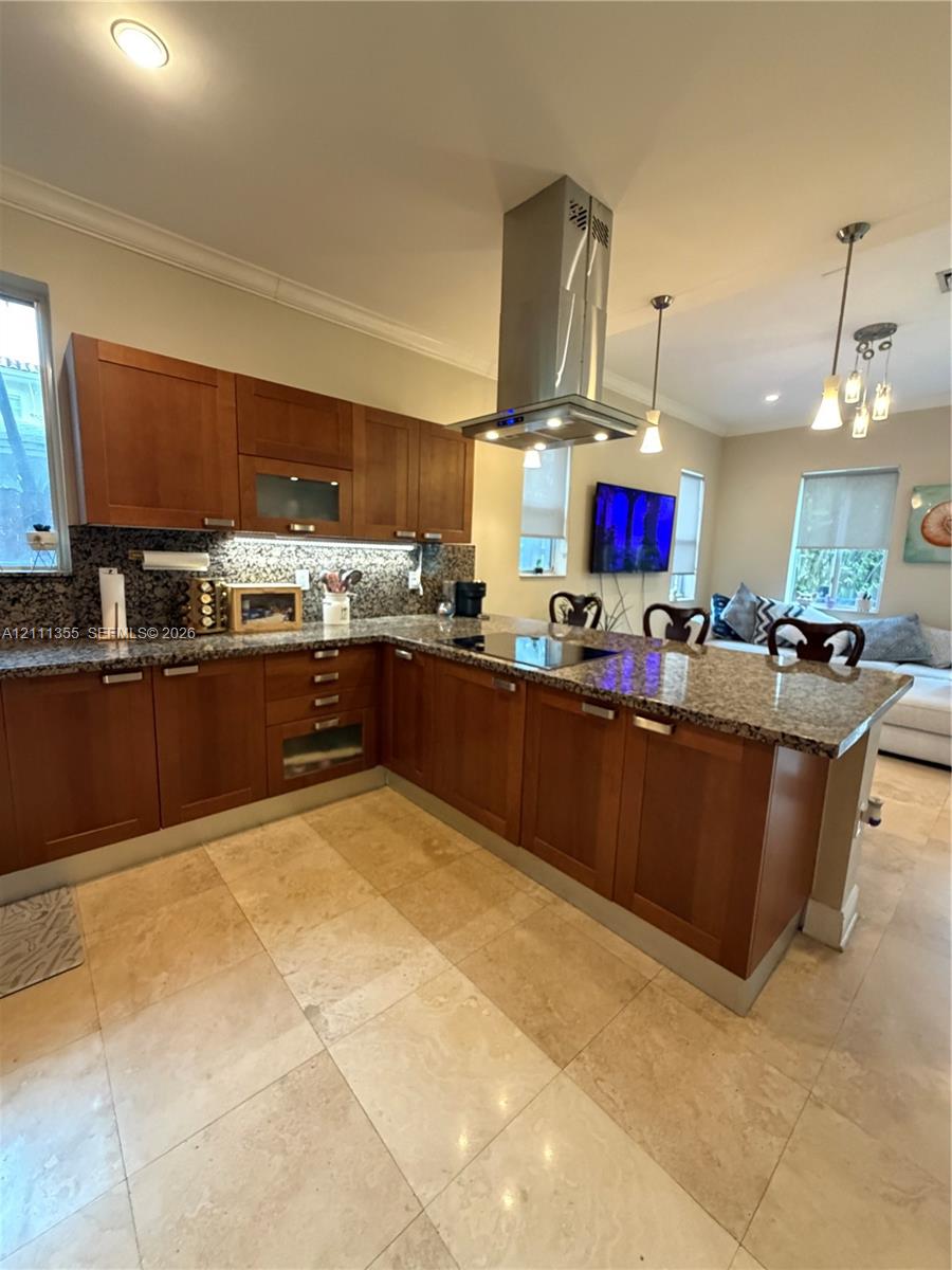 Kitchen featuring shaker-style wood cabinetry, stone countertops, stainless steel chimney-style range hood, integrated cooktop, and neutral stone tile flooring