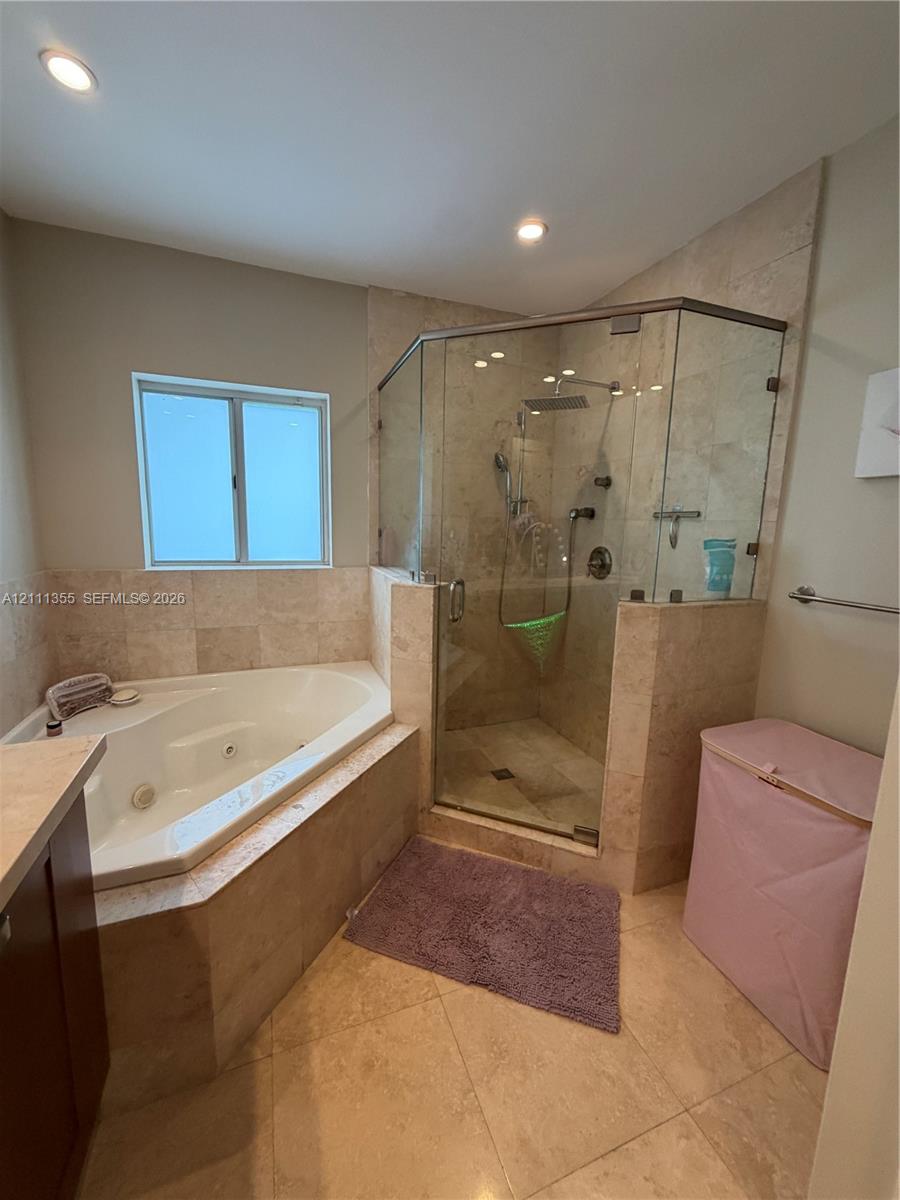 Jetted soaking tub and walk-in shower with a glass enclosure and wall-mounted rainfall showerhead, complemented by neutral-toned stone tile flooring and wall surrounds