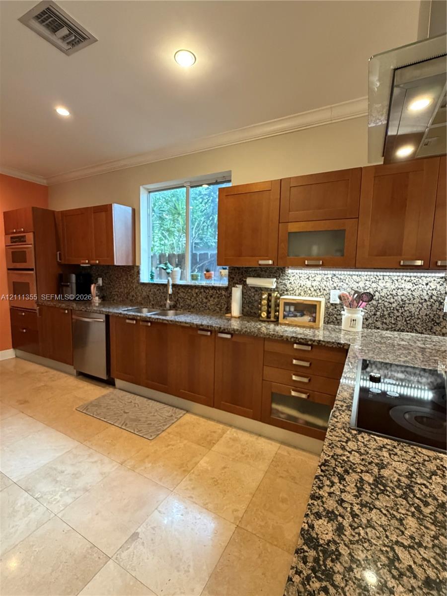 Kitchen featuring wooden cabinetry, stone-surface countertops, stone tile flooring, integrated double oven, and stainless steel dishwasher