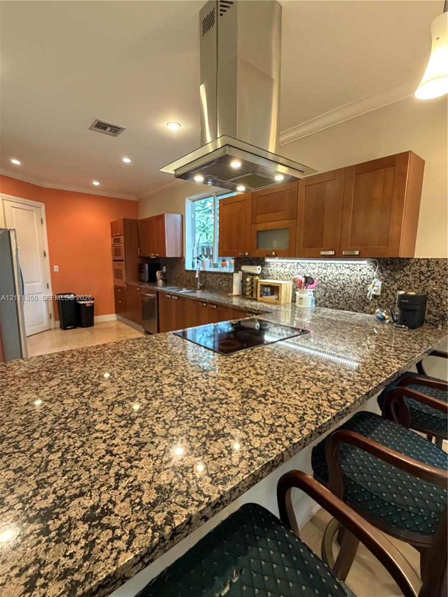 Kitchen featuring a stone-surface island, stainless steel chimney-style range hood, recessed lighting, wood cabinetry, and under-cabinet lighting