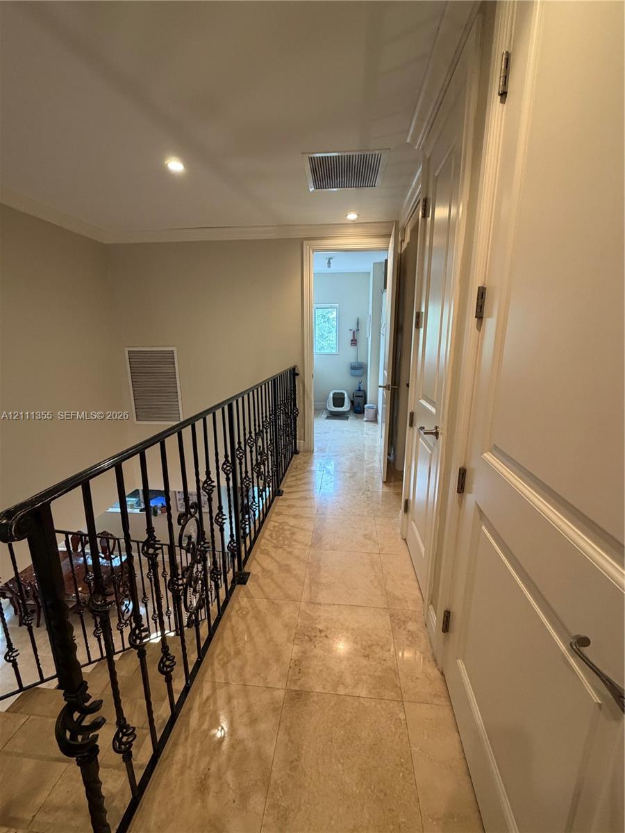 Hallway featuring stone-finish tile flooring, decorative wrought-iron railings, recessed lighting, and multi-panel doors with metallic hardware
