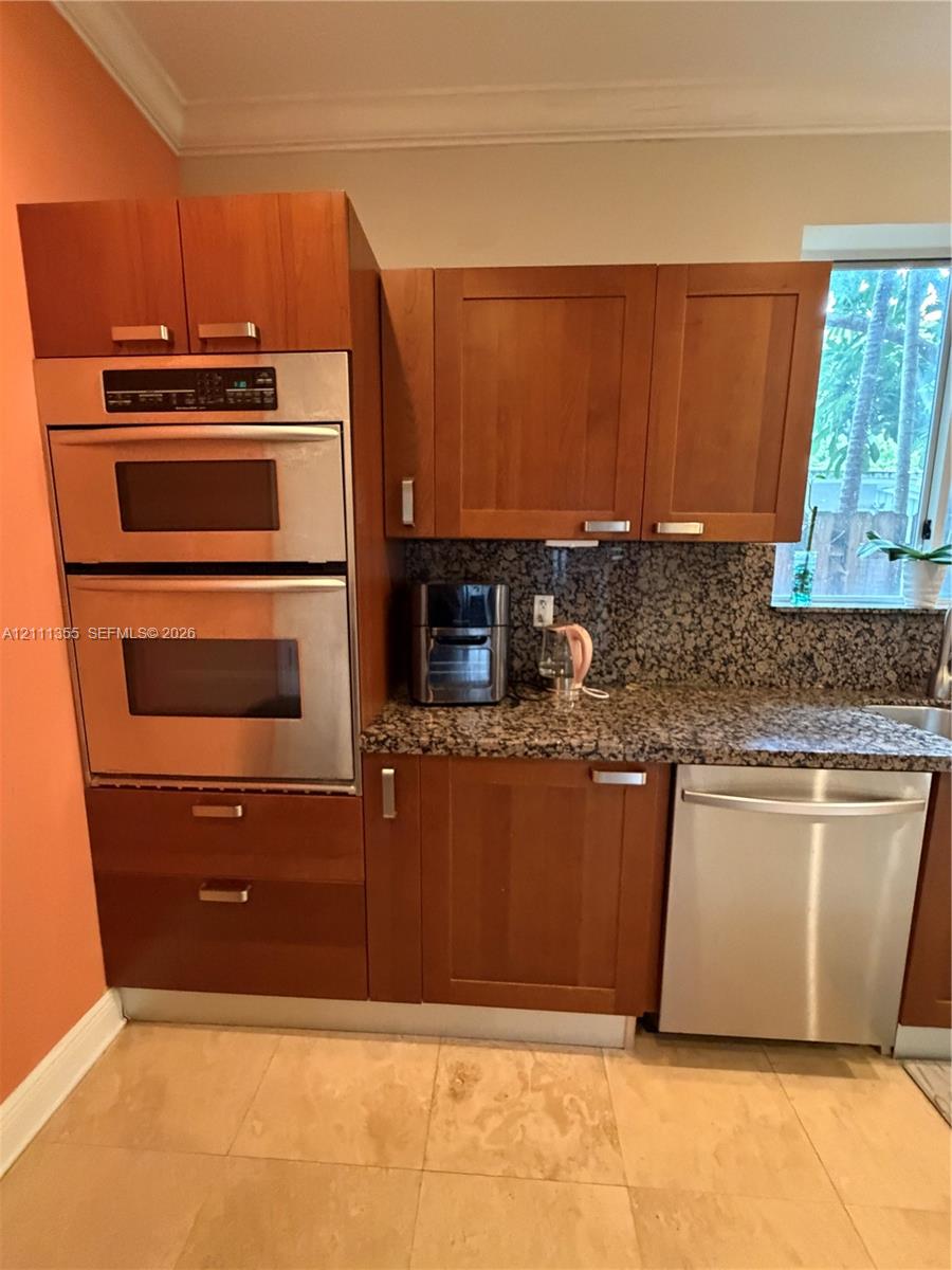 Kitchen featuring wood cabinetry, stone countertops, stainless steel double wall oven, stainless steel dishwasher, and large-format tile flooring
