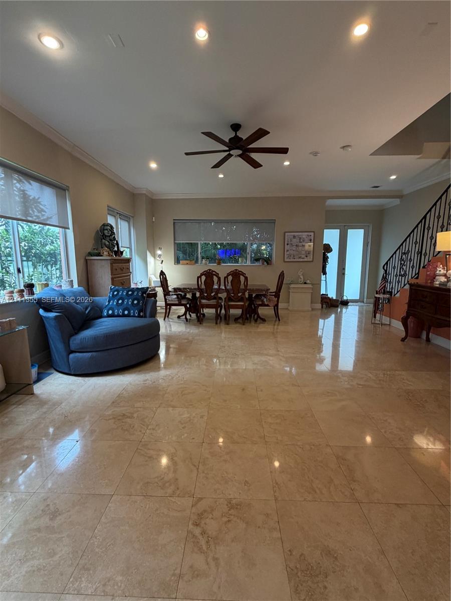 Large-format natural stone flooring, recessed ceiling lighting, a multi-blade ceiling fan, and a staircase featuring decorative metal balusters
