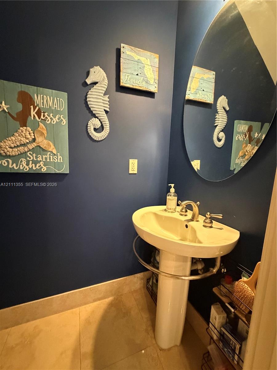 Pedestal sink featuring a polished chrome faucet and an oval wall-mounted mirror set against navy blue walls and neutral floor tile