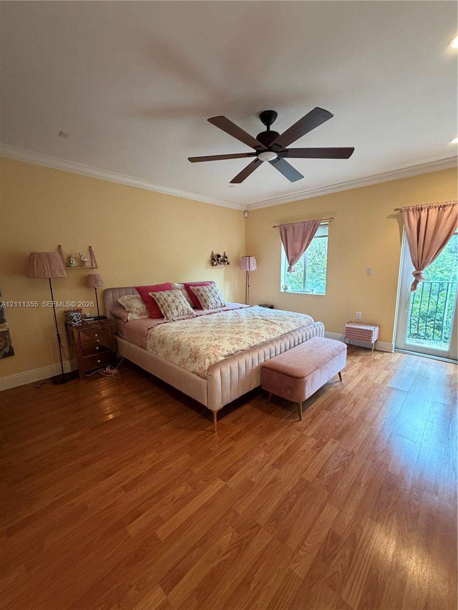 Wood-finish flooring, ceiling fan with integrated light, crown molding, and glass-paned door opening to an exterior balcony