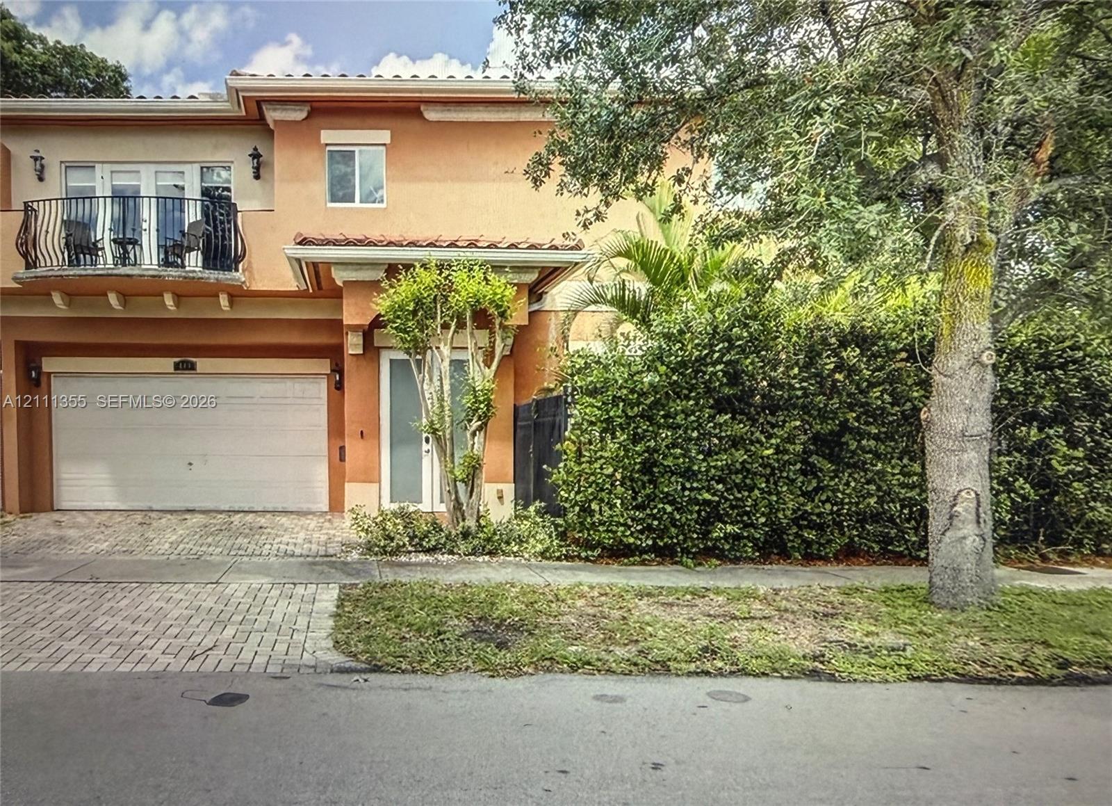 Stucco exterior featuring an arched second-story balcony with metal railing, a paved driveway, and covered entryway Stucco exterior featuring an arched second-story balcony with metal railing, a paved driveway, and covered entryway