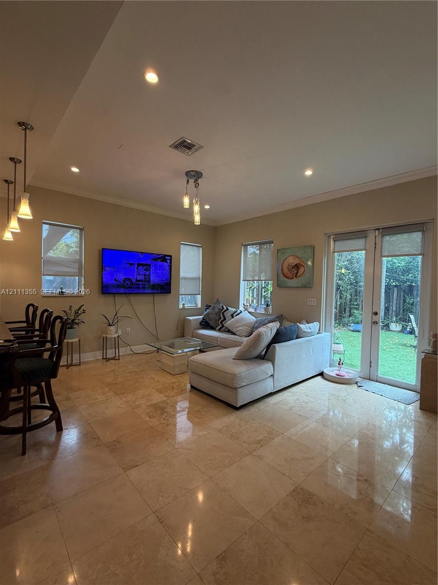 Open floor plan interior featuring polished stone tile flooring, multi-pane glass door leading to exterior space, recessed lighting, and crown molding