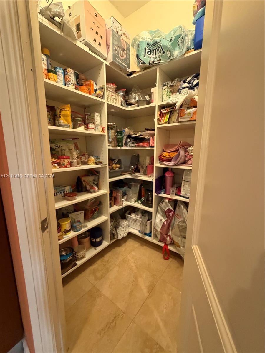 Walk-in pantry featuring white wrap-around shelving and neutral tile flooring