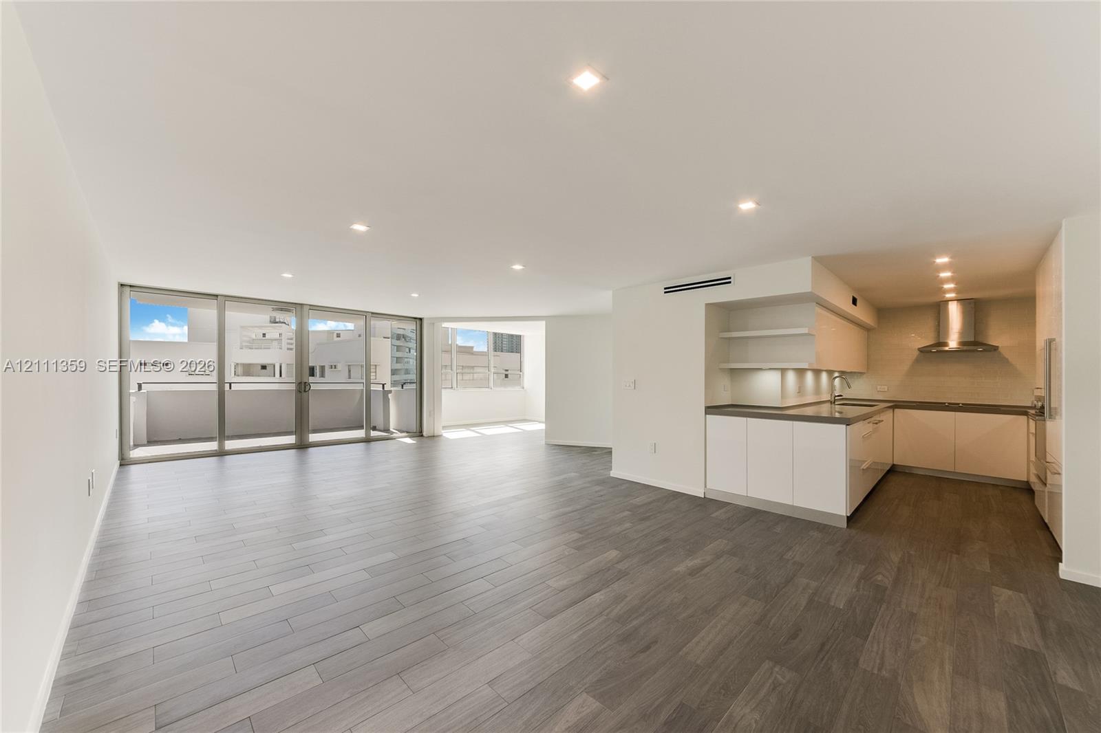 Open floor plan featuring wood-finish flooring, recessed lighting, floor-to-ceiling glass doors, and a kitchen equipped with cabinetry, stone-surface countertops, and a stainless steel range hood