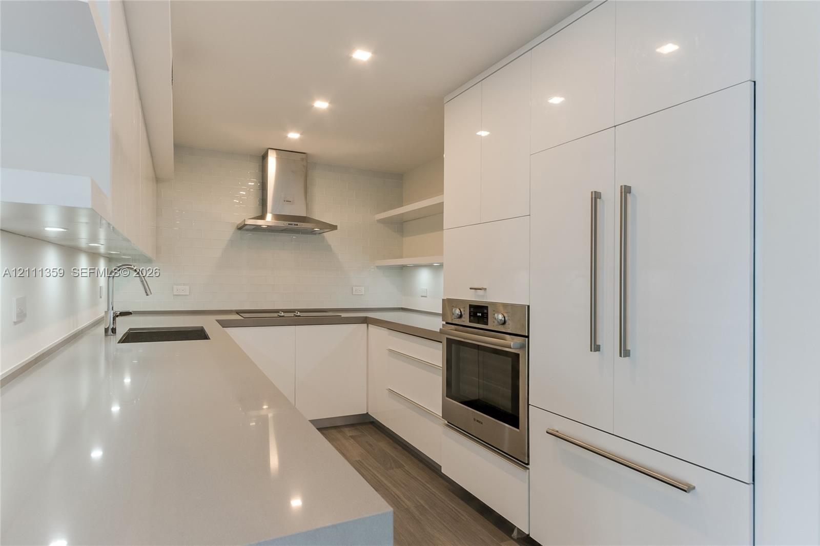 Kitchen featuring white high-gloss cabinetry, solid surface countertops, stainless steel appliances, open shelving, and wood-finish flooring