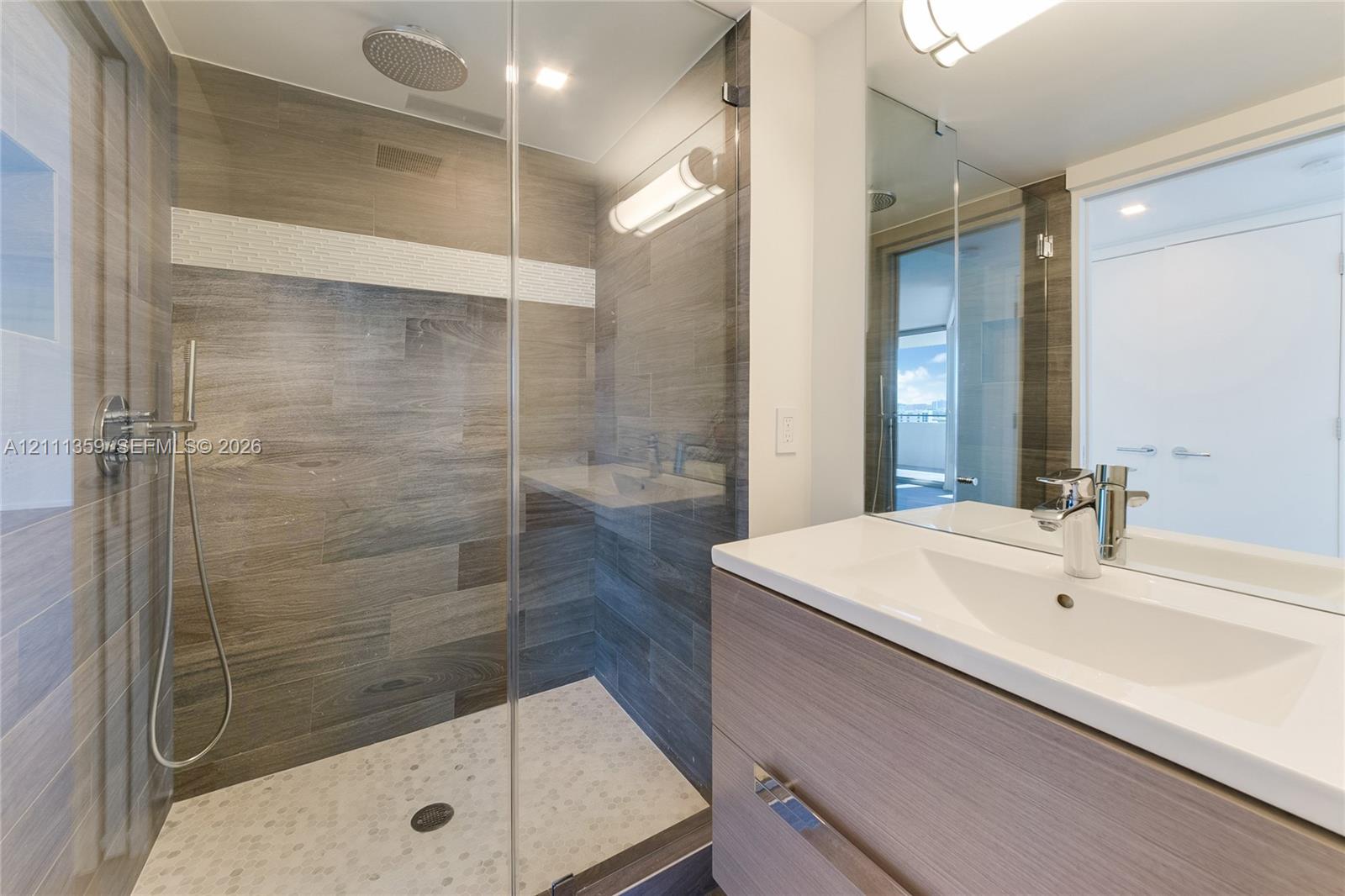 Bathroom featuring a glass-enclosed walk-in shower with stone tile flooring, wall-mounted rainfall showerhead, and handheld sprayer