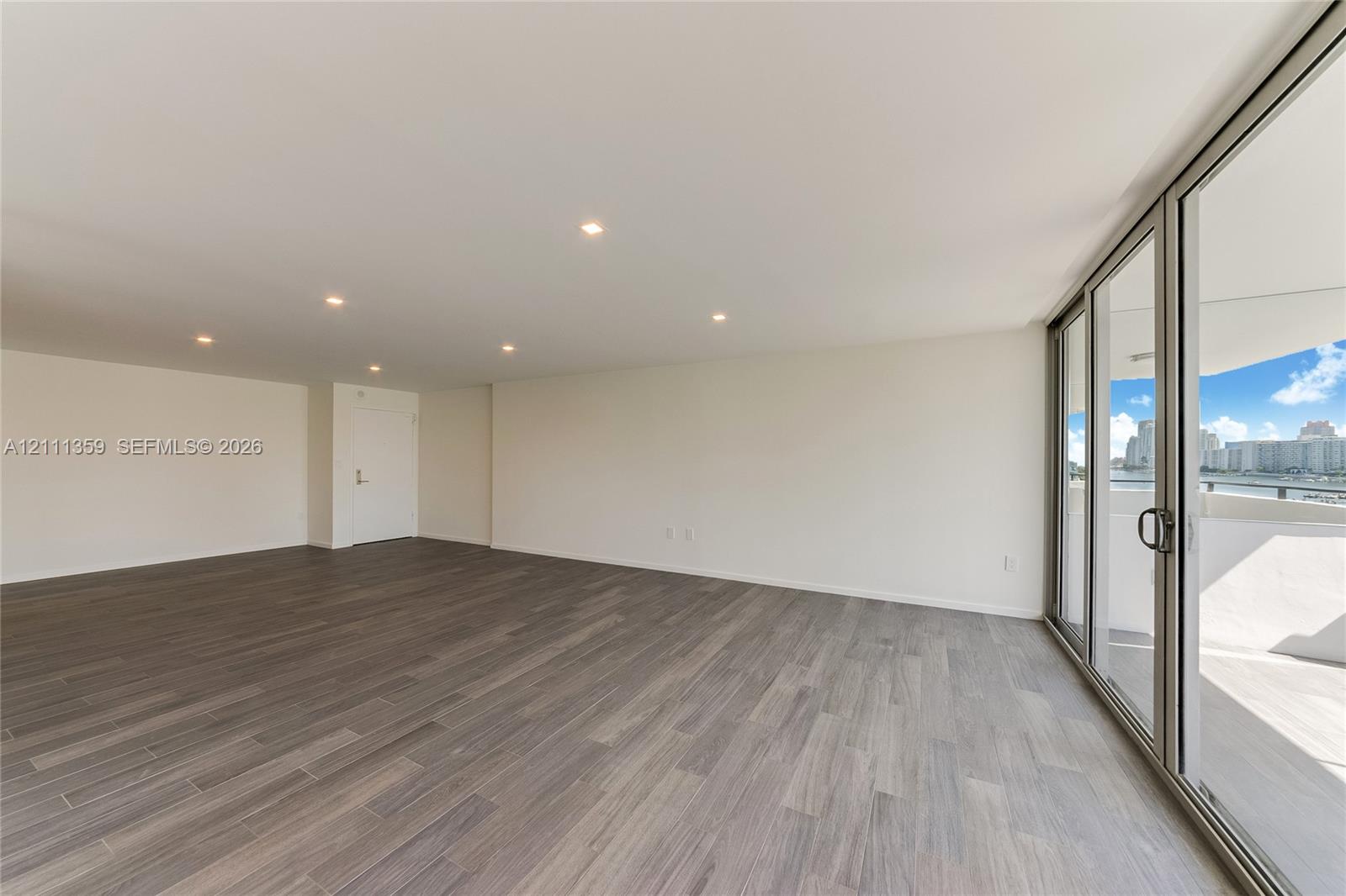 Open-concept living space featuring wood-finish flooring, recessed ceiling lighting, and floor-to-ceiling glass sliding doors leading to an outdoor balcony