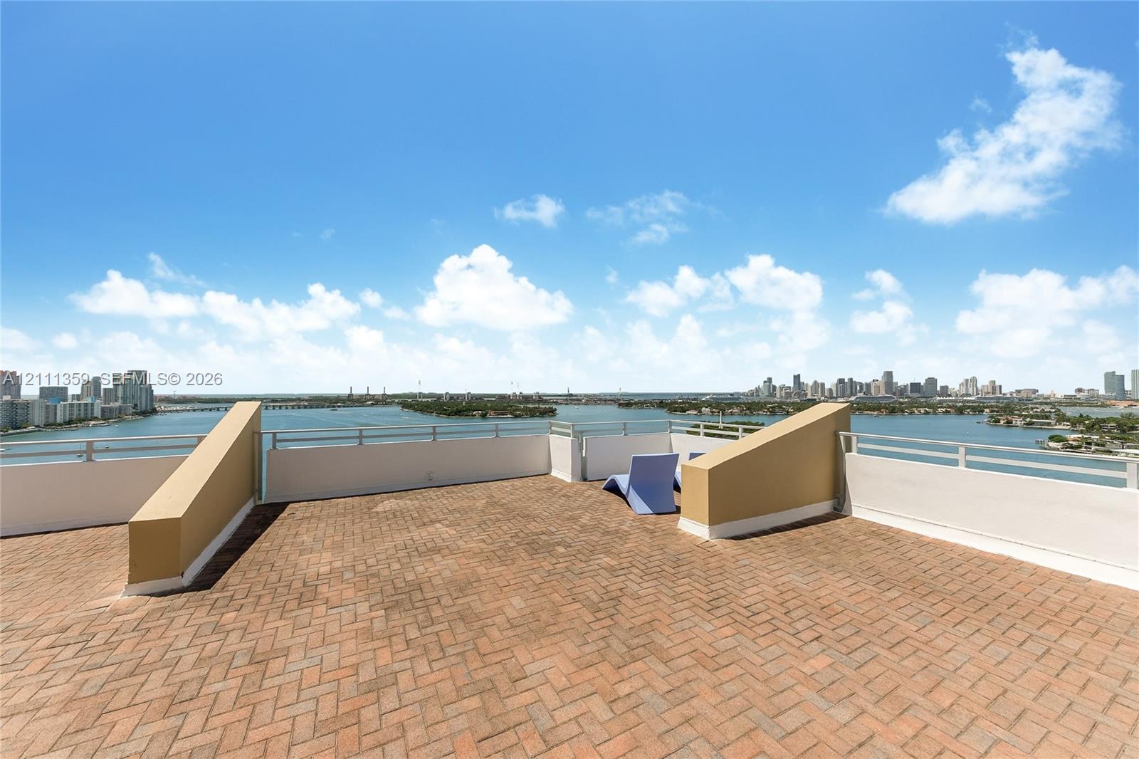 Expansive rooftop terrace featuring terracotta-style brick pavers, integrated solid-surface perimeter walls, and metal railings